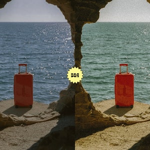 May include: A red suitcase sits on a rocky ledge overlooking the ocean. The suitcase has a handle and wheels. The ocean is a deep blue color. The sky is a light blue color. The rocks are a brown color.