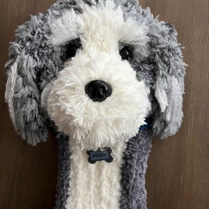 May include: A plush dog headcover in shades of gray and white, with a black nose and eyes. The headcover has a tag that reads "PERCY". The dog's fur is soft and textured, and the headcover is designed to fit over a golf club.