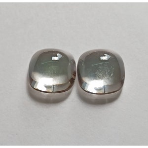 May include: Two clear, faceted, cushion-shaped gemstones with a slight iridescent shimmer.