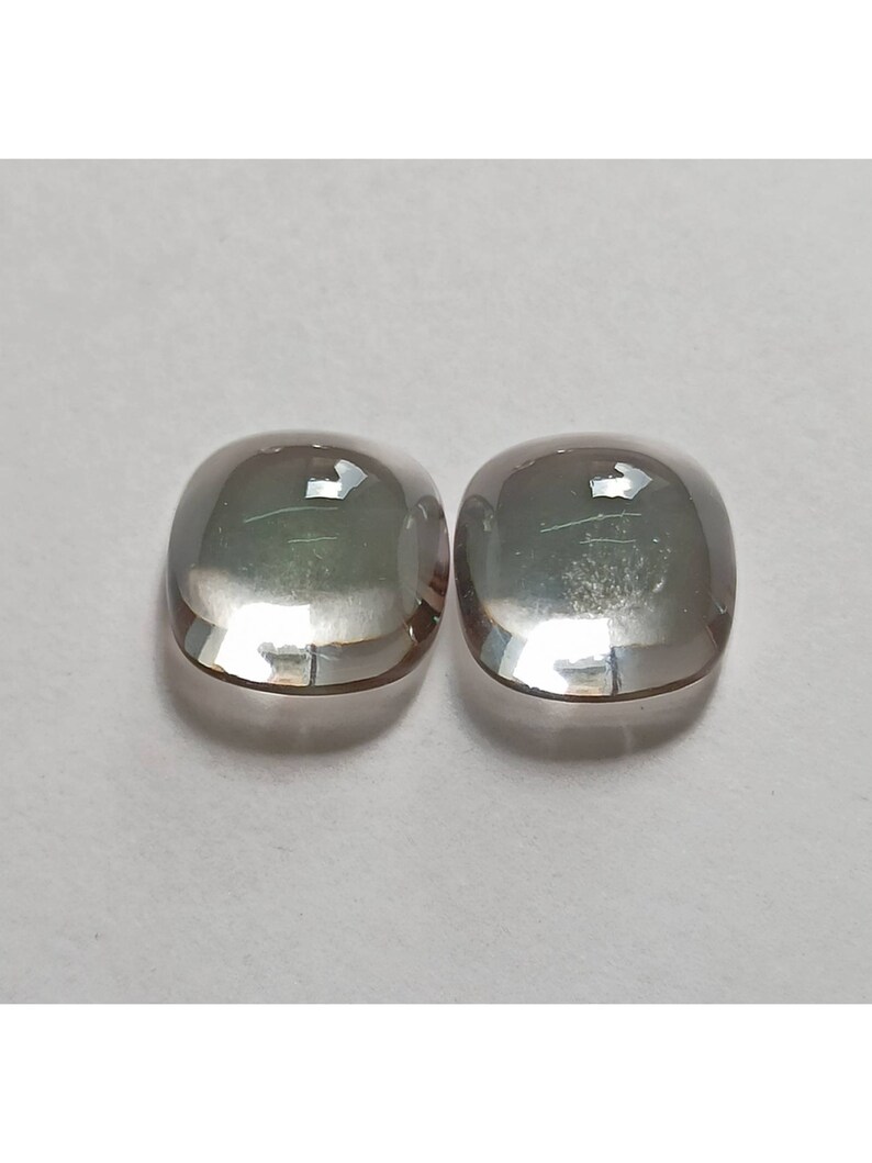 May include: Two clear, faceted, cushion-shaped gemstones with a slight iridescent shimmer.