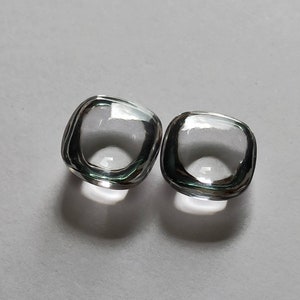 May include: Two clear glass square-shaped cabochons with a beveled edge.