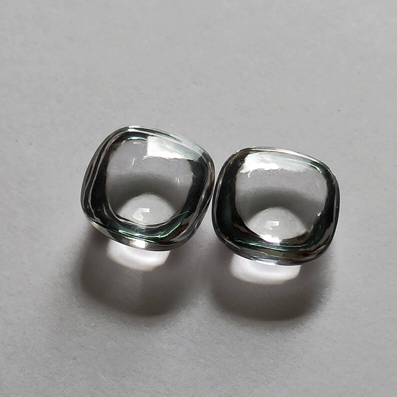 May include: Two clear glass square-shaped cabochons with a beveled edge.