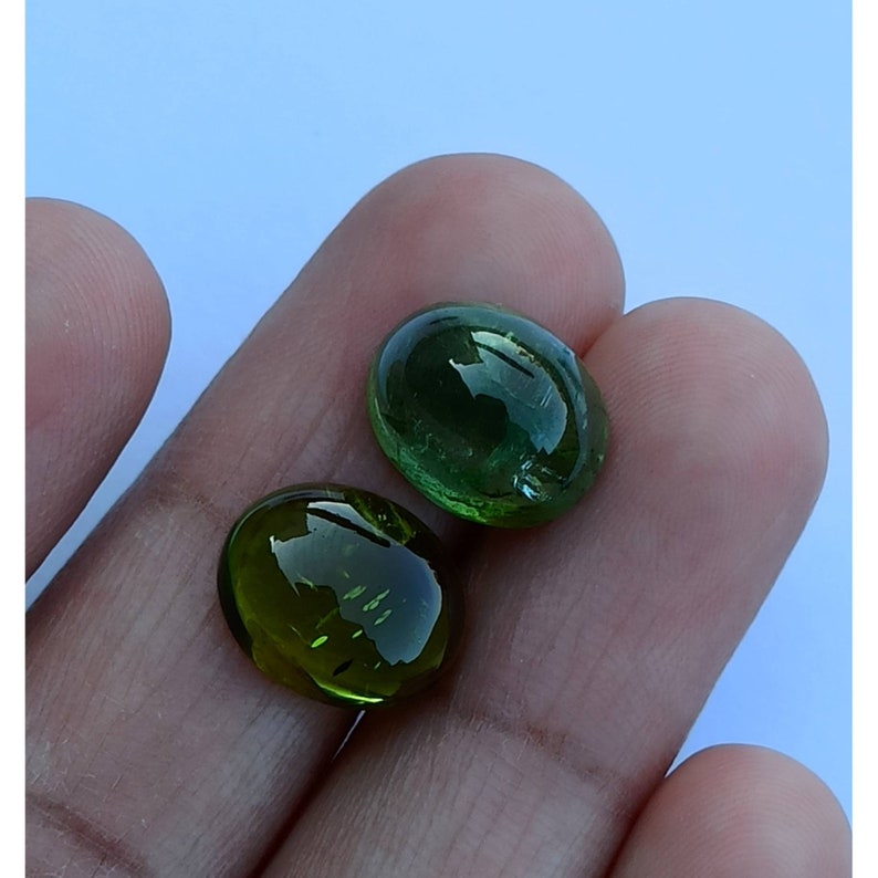 May include: Two green oval-shaped gemstones with a smooth, polished finish. The stones are translucent and have a slight shimmer.