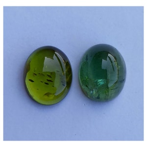 May include: Two round, green gemstones, one a darker green with a more opaque appearance, and the other a lighter green with a more translucent appearance.