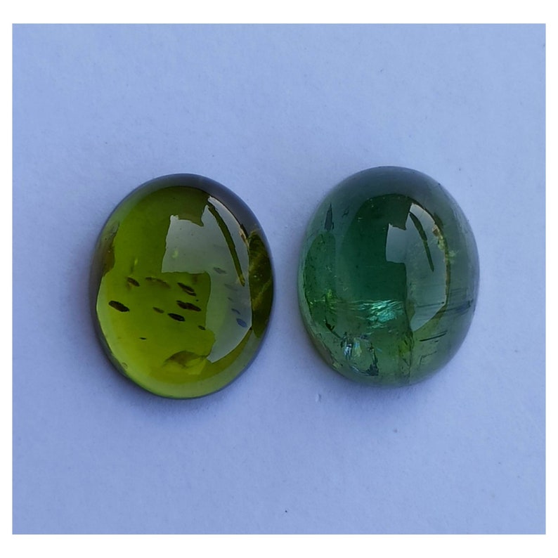 May include: Two round, green gemstones, one a darker green with a more opaque appearance, and the other a lighter green with a more translucent appearance.