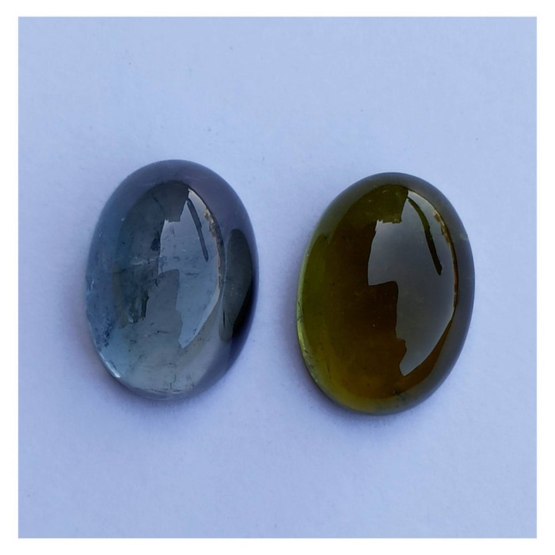 May include: Two oval-shaped gemstones, one blue and one green, on a white background.
