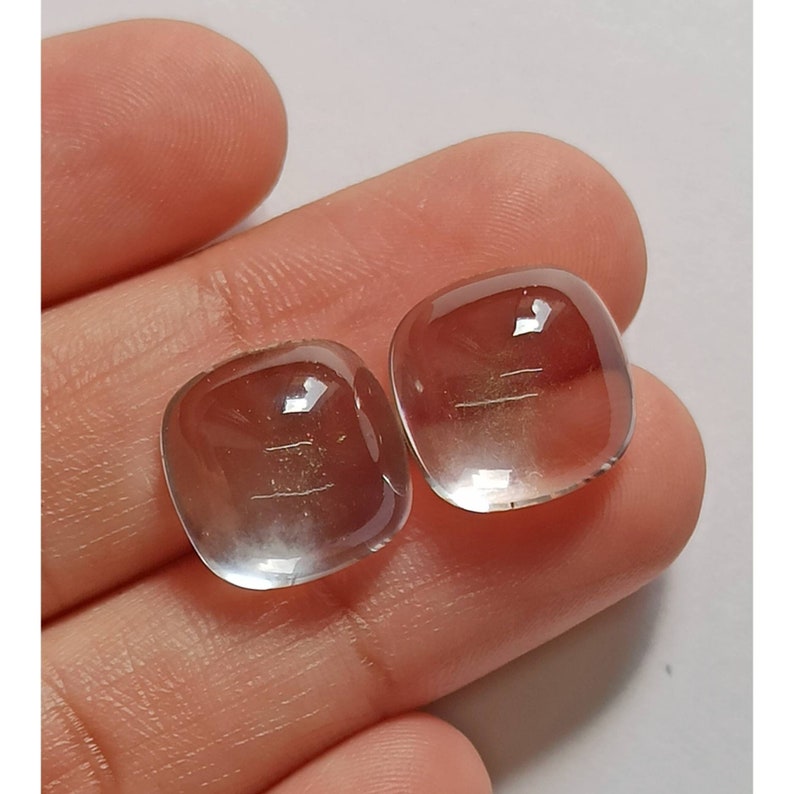 May include: Two clear, faceted, cushion-shaped gemstones with a slight golden hue. The stones are approximately 1 inch in size.