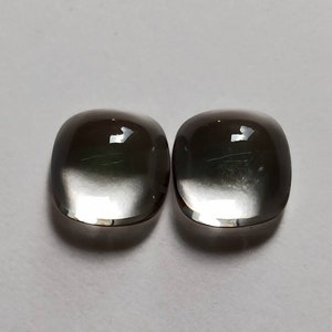 May include: Two oval-shaped, clear, faceted gemstones with a dark gray to black color gradient. The stones are smooth and polished.