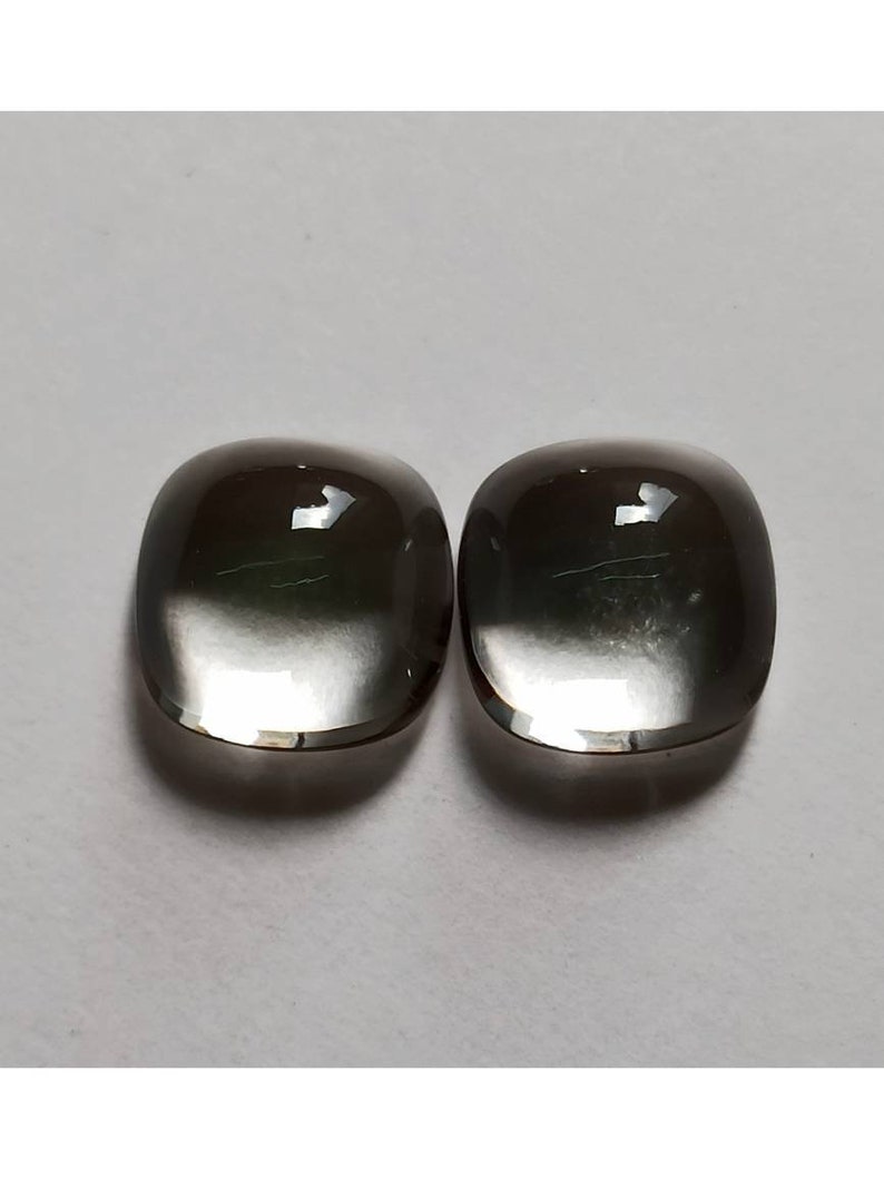 May include: Two oval-shaped, clear, faceted gemstones with a dark gray to black color gradient. The stones are smooth and polished.