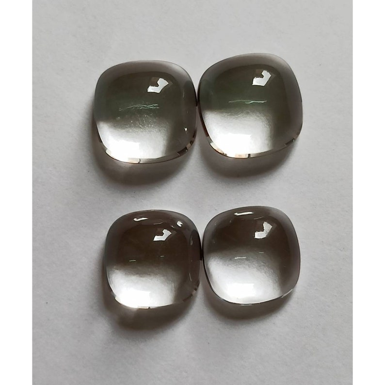 May include: Four clear, faceted, cushion-shaped gemstones with a smoky gray hue. The stones are arranged in two pairs, side by side.
