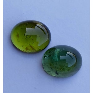 May include: Two oval-shaped green gemstones with a smooth, polished finish. The gemstones have a translucent appearance with visible internal inclusions.