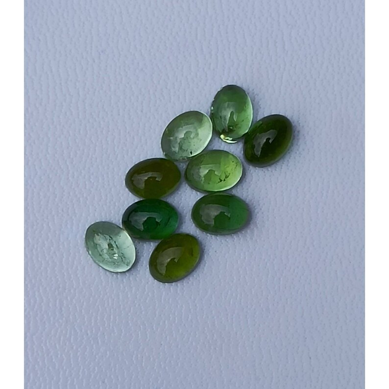 May include: A group of ten oval-shaped green gemstones. The gemstones are translucent and have a slight shimmer.
