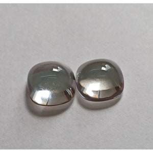 May include: Two clear, faceted, cushion-shaped gemstones with a slight iridescent shimmer.
