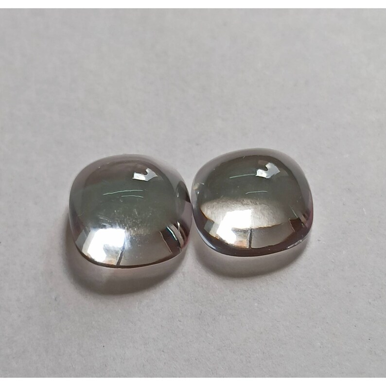 May include: Two clear, faceted, cushion-shaped gemstones with a slight iridescent shimmer.