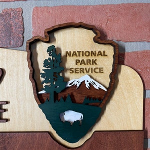 May include: A wooden sign with the words "Welcome to Nature" and a green, brown, and white National Park Service logo. The logo features a mountain, a tree, and a bison.