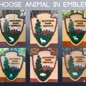 May include: Six wooden signs with the National Park Service logo. Each sign features a different animal: a fish, a wolf, a moose, a person, a bison, and a bear.
