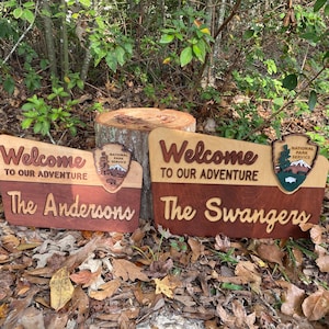 May include: Two wooden welcome signs with the text "Welcome to our adventure" and the family names "The Andersons" and "The Swangers". Each sign features a National Park Service logo with a mountain scene.