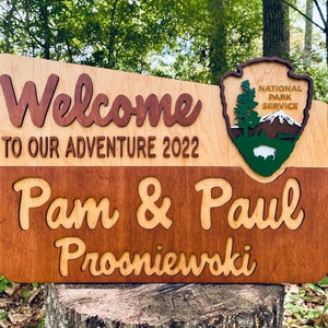 May include: Welcome to our adventure 2022 sign with a wood-burned National Park Service logo and the names Pam & Paul Prosniewski.