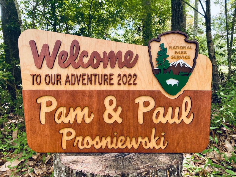 May include: Welcome to our adventure 2022 sign with a wood-burned National Park Service logo and the names Pam & Paul Prosniewski.