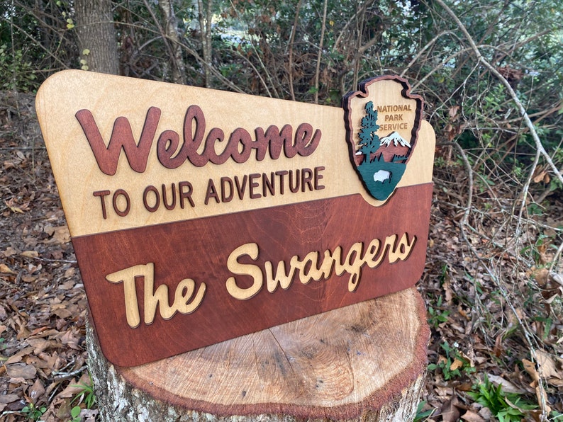 May include: A wooden sign with the text "Welcome to our adventure The Swangers" and the National Park Service logo. The sign is made of two different types of wood, one light and one dark.