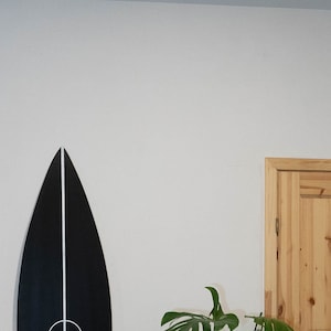 May include: Two surfboards hanging on a white wall, one is black with a white circle and line, the other is red and white striped. A green chair and a potted plant are in the foreground.