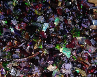 May include: A close-up of a pile of iridescent black opal chips. The chips are various sizes and shapes, with a mix of green, red, and purple hues.