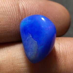 Pode incluir: Uma gema de opala azul com uma forma redonda e lisa. A opala tem uma cor azul brilhante com flashes de branco iridescente.