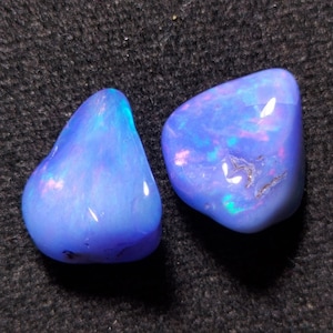 Pode incluir: Duas pedras de opala azul com reflexos iridescentes de cor. As pedras são lisas e têm uma forma arredondada.