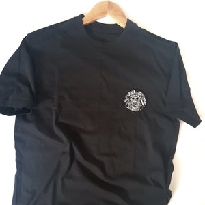 May include: Black t-shirt with a white graphic of a skull wearing a headdress on the left chest.