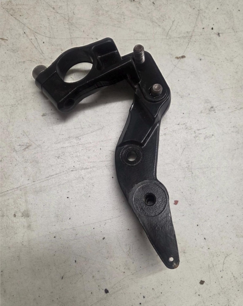 K&ouml;nnte beinhalten: Ein schwarzes mechanisches Metallteil mit einer kreisf&ouml;rmigen &Ouml;ffnung und mehreren Befestigungspunkten. Die Komponente hat ein Scharnierdesign mit einem Bolzen und einem abgerundeten Ende. Das Objekt ist wahrscheinlich Teil einer gr&ouml;&szlig;eren Maschine oder eines Mechanismus.