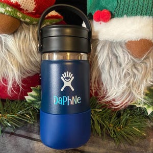 A blue and black insulated water bottle with a handle, placed on a surface with Christmas decorations and gnomes in the background.