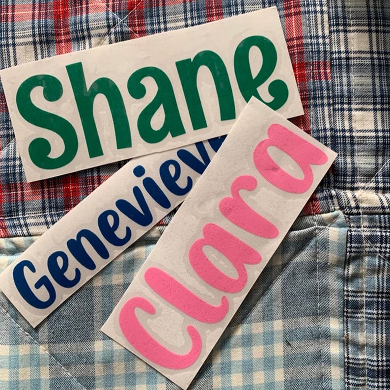 three stickers with names on them, placed on a plaid fabric background.