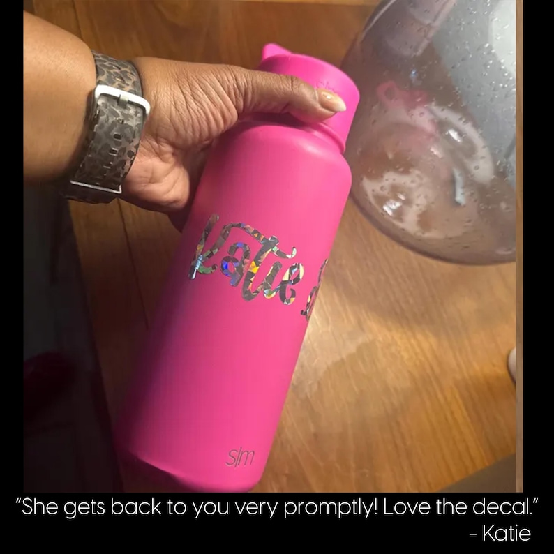 A person's hand holding a pink water bottle with a personalized decal, and a glass container in the background.