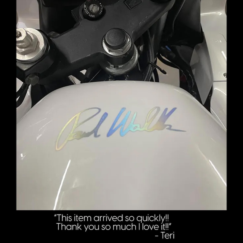 a close-up view of a white motorcycle, focusing on the gas tank with a signature or logo on it.