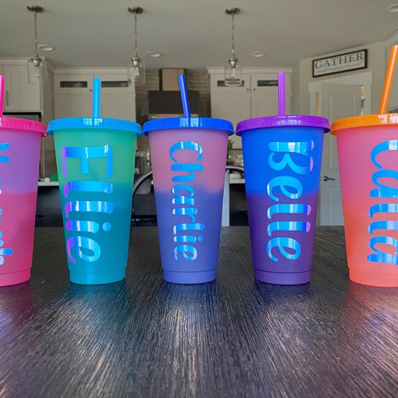A row of colorful personalized cups with names on them, placed on a wooden surface.