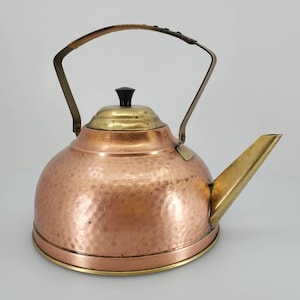 Könnte beinhalten: Ein gehämmerter Kupferkessel mit einem Messingdeckel und einem Messingausguss. Der Kessel hat einen Messinggriff mit einem schwarzen Knopf.