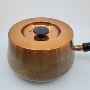 May include: A copper saucepan with a lid and a black handle. The saucepan has a hammered finish and a patina.