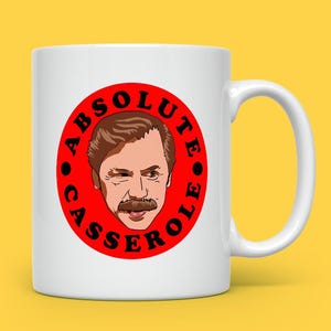 May include: White ceramic mug with a red circle design featuring a cartoon illustration of a man with a mustache and the text "ABSOLUTE CASSEROLE" in black. The mug has a curved handle and is set against a yellow background.