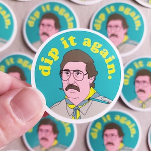 May include: A round sticker with a teal background and white border. The sticker features a cartoon illustration of a man with brown hair and a moustache wearing a green shirt and a yellow scarf. The text "dip it again." is written in yellow letters on the sticker.