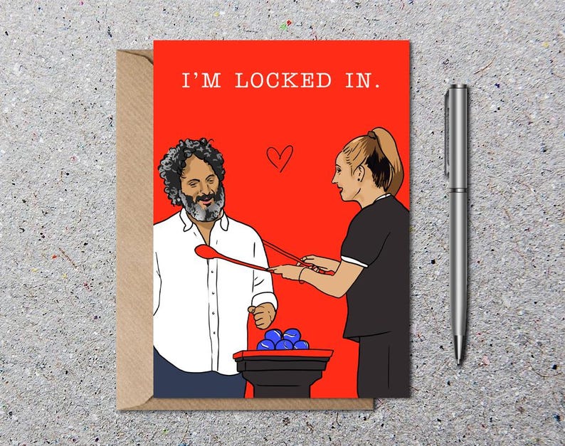 May include: Greeting card with the text "I'M LOCKED IN." on a red background. The card features an illustration of two people and a heart. A silver pen rests on the surface next to the card.