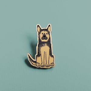 May include: A wooden pin of a brown and black German Shepherd dog sitting with its tongue out. The dog is wearing a black collar with a silver tag.