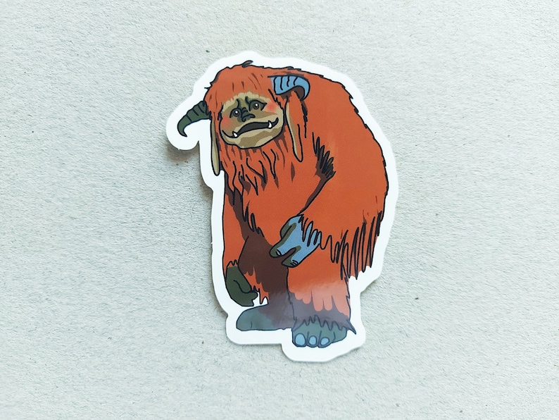 May include: A sticker featuring a cartoon orange furry creature with blue hands and a horn. The creature has a sad expression and is standing on two legs.