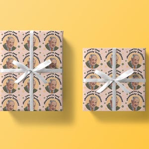 May include: Pink and white wrapping paper with a repeating pattern of a man's face and the text "You're just absolutely brilliant".
