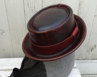 May include: A brown leather fedora hat with a wide brim and a brown leather band. The hat is distressed and has a vintage look.