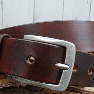 May include: A brown leather belt with a silver buckle. The belt has multiple holes for adjusting the size.
