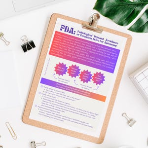 May include: A clipboard with a printed document about Pathological Demand Avoidance (PDA). The document has a purple and orange gradient header and includes text, diagrams, and bullet points. The clipboard is on a white surface with office supplies.