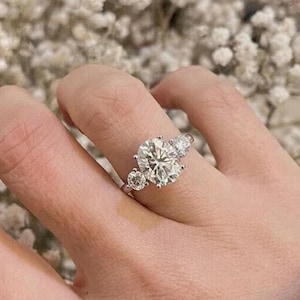May include: A silver ring with a large round diamond in the center and two smaller diamonds on either side.