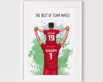 Op de afbeelding: Een ingelijste print met een vader en kind in rode voetbalshirts. Het kind zit op de schouders van de vader, met de tekst "THE BEST OF TEAM MATES" erboven. Het shirt van het kind heeft "DILLON" en "19", dat van de vader "DADDY" en "1".