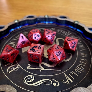 May include: A set of six red polyhedral dice with black dinosaur-themed numbering and graphics, resting on a circular dark brown wooden tray featuring gold text that reads "OCTOPUS APPROVES OF YOUR ROLLS" and a central octopus illustration.
