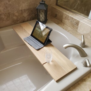 May include: A light-colored wooden bathtub tray with a tablet and a glass of water. The tablet is in a gray case and is propped up on the tray. A black lantern sits in the background.